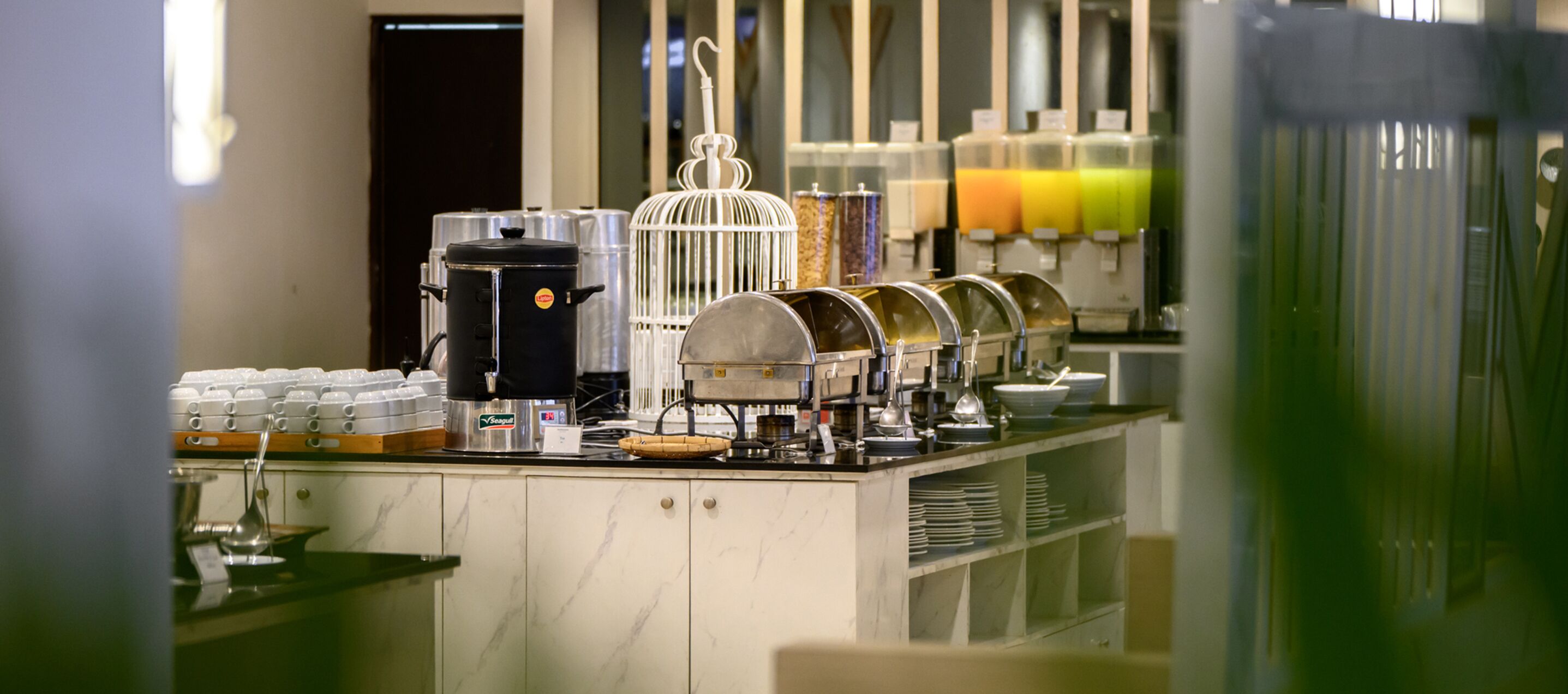 A buffet setup with various food containers, a coffee machine, and a juice dispenser.