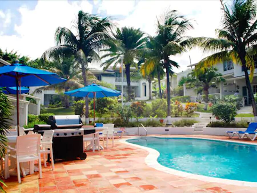 A pool area with lounge chairs, a barbecue grill, and palm trees.
