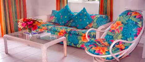 A living room with a sofa and a chair, a glass coffee table, and a vase of flowers.
