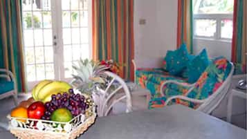 A room with a dining table, a wicker fruit basket, and a chair with a colorful cushion.