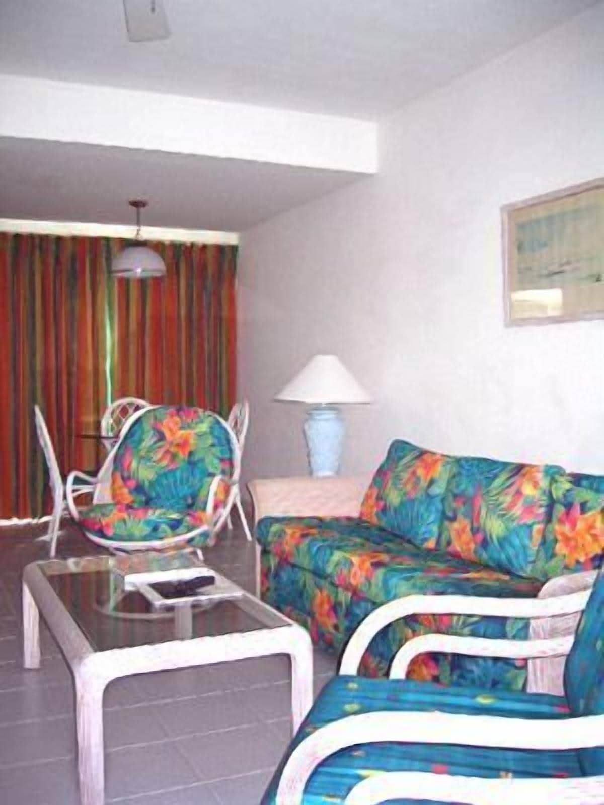 Un salon avec un canapé, des fauteuils, une table basse en verre et une lampe.