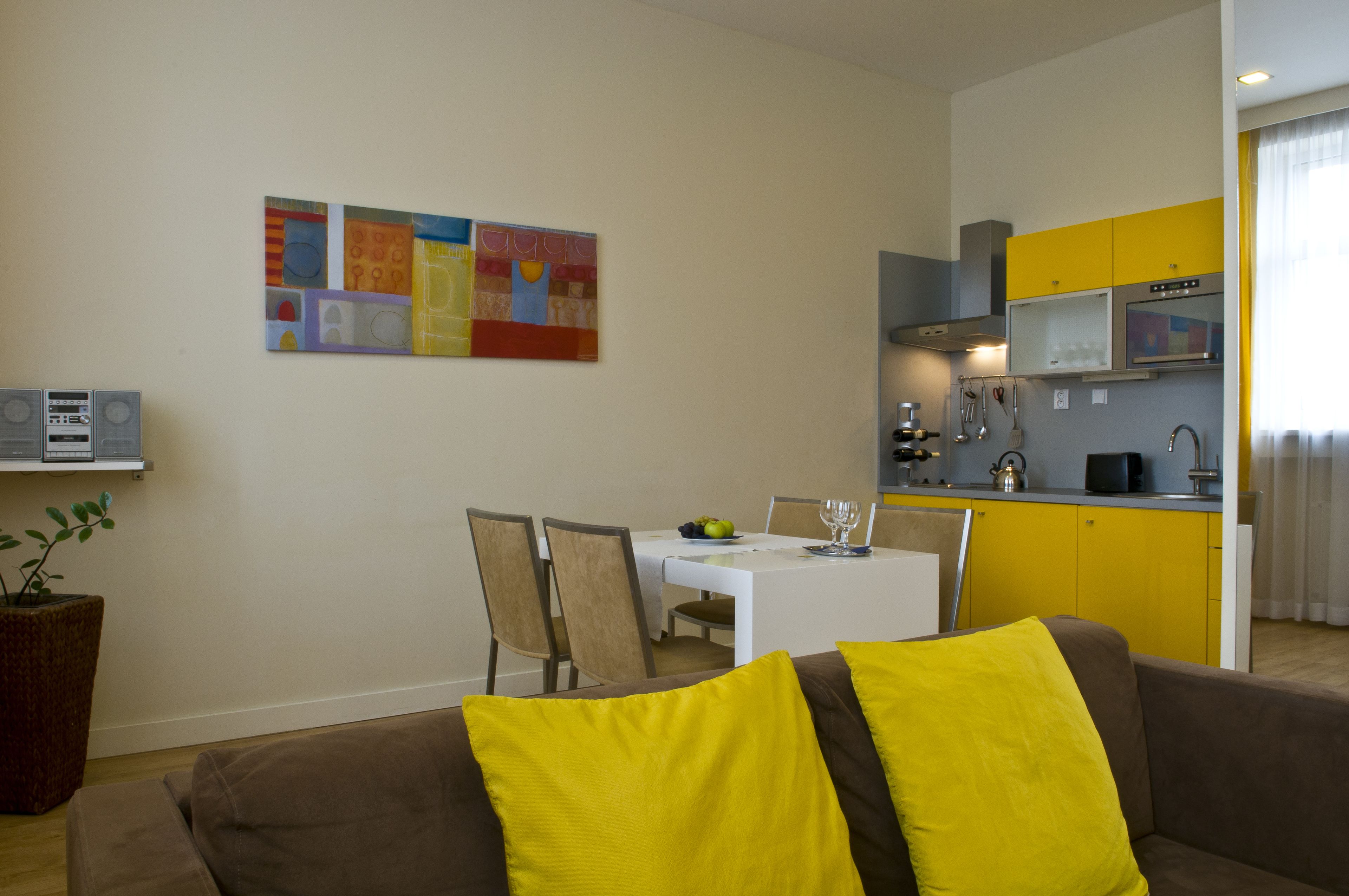 Un espacio habitable compacto con comedor, kitchenette y un sofá con cojines amarillos.