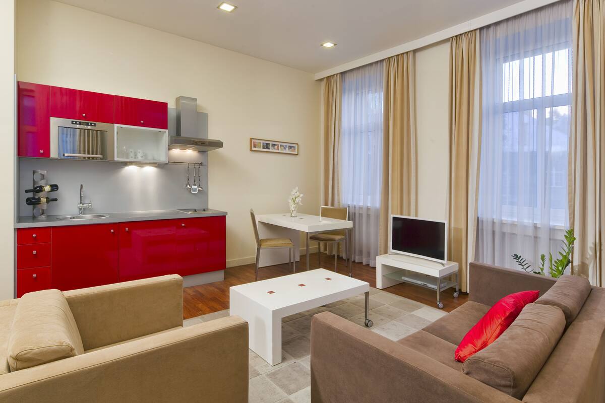 Una sala de estar moderna con una cocina roja, una mesa de comedor blanca, un sofá y un televisor.