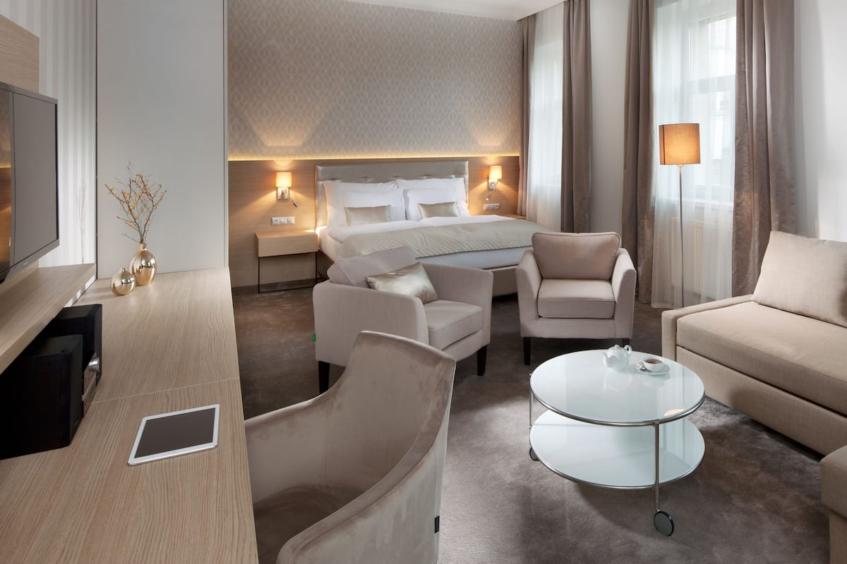 Una habitación de hotel moderna con una cama, dos sillones, un sofá, una mesa de centro de vidrio y una televisión.