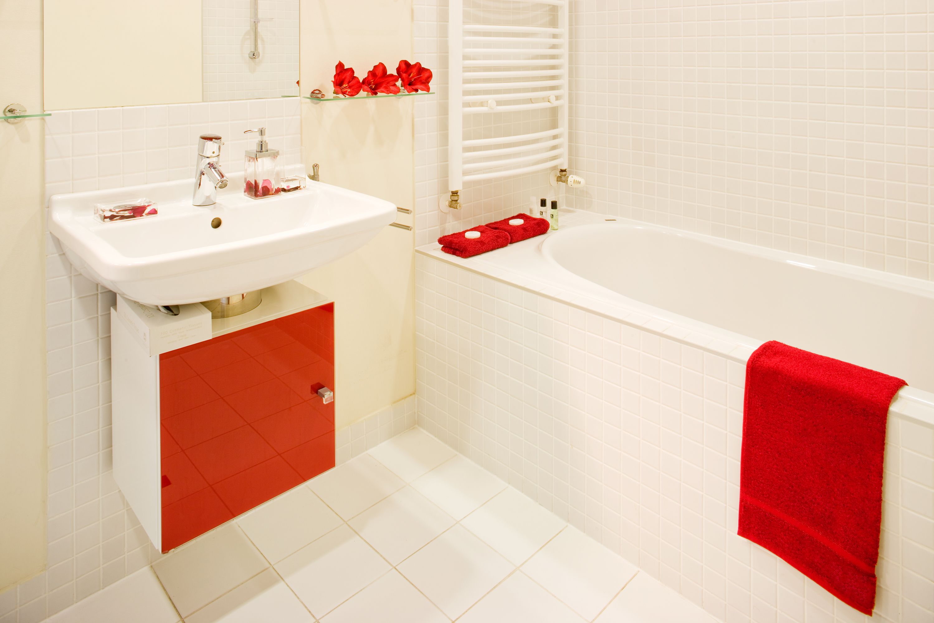 Une salle de bain avec un lavabo blanc, un meuble rouge et une baignoire agrémentée d’une serviette rouge.