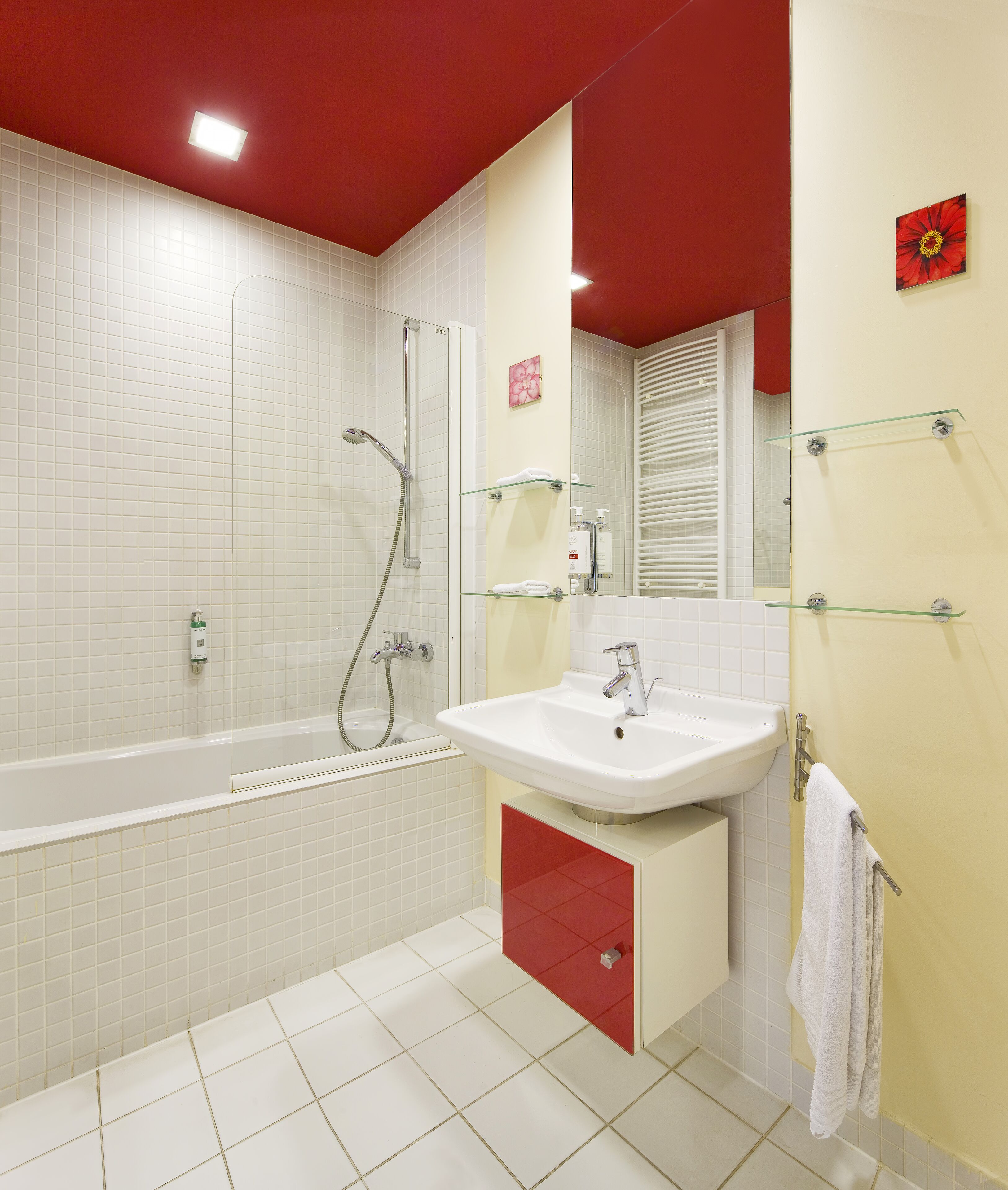 Un baño moderno con una bañera blanca, un lavamanos con espejo y una pared de acento roja.