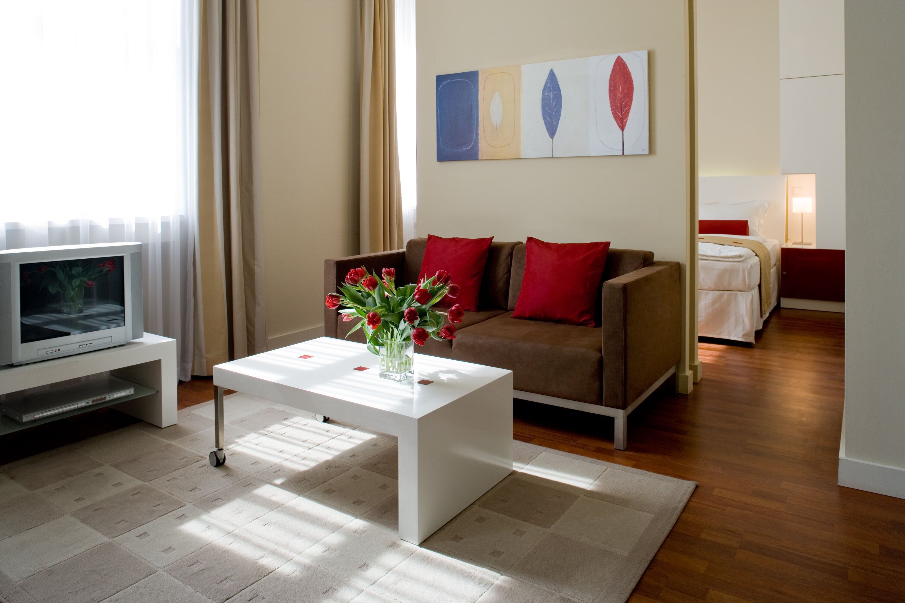 Un salon moderne avec une table basse blanche, des coussins rouges, un téléviseur et un tableau accroché au mur.