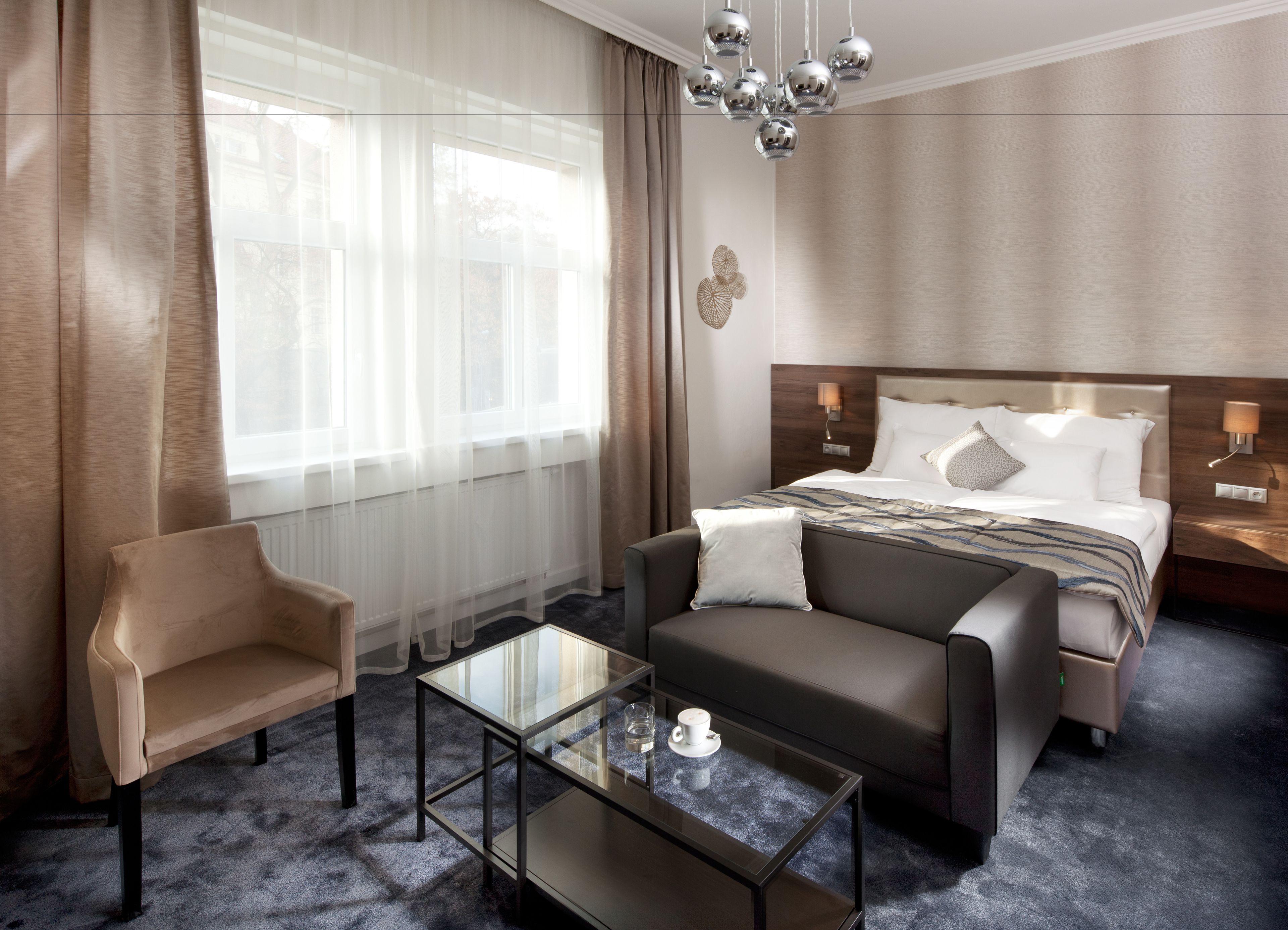 A modern hotel room with a bed, a sofa, a glass coffee table, and a chair.