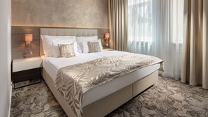 Una habitación de hotel moderna con una cama grande, dos mesitas de noche con lámparas, un cabecero y una alfombra estampada.