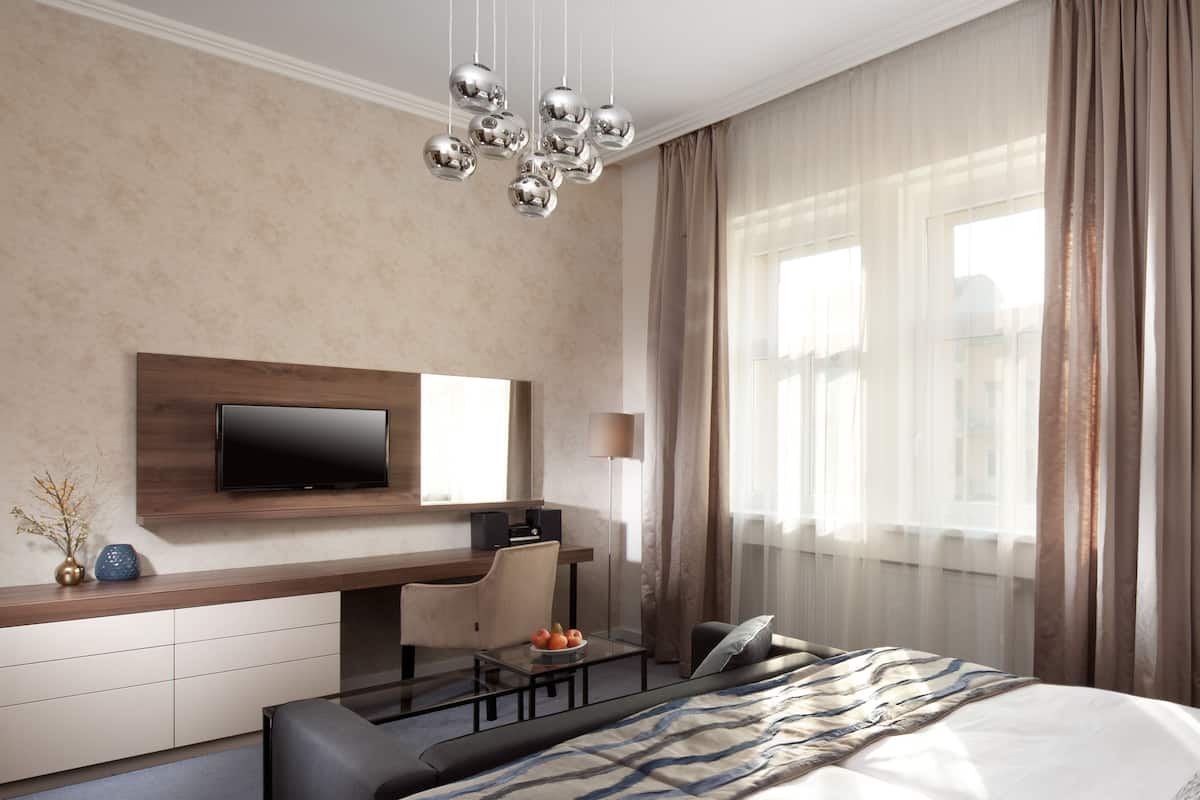 Habitación de hotel moderna con una cama grande, un escritorio con silla, un televisor de pantalla plana montado en la pared y un ventanal con cortinas.