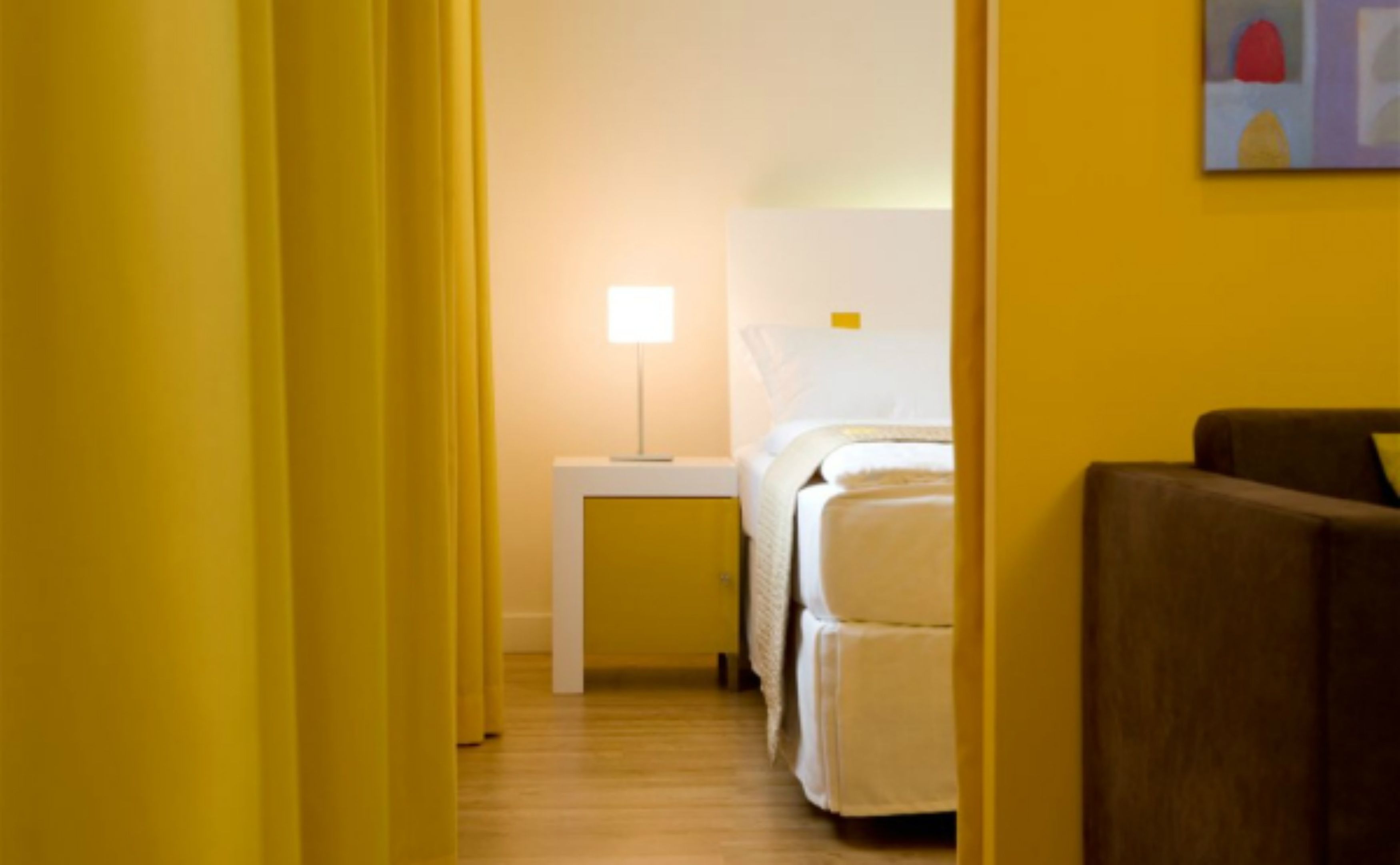 Ett hotellrum med en säng, ett sängbord med en lampa och en brun fåtölj.