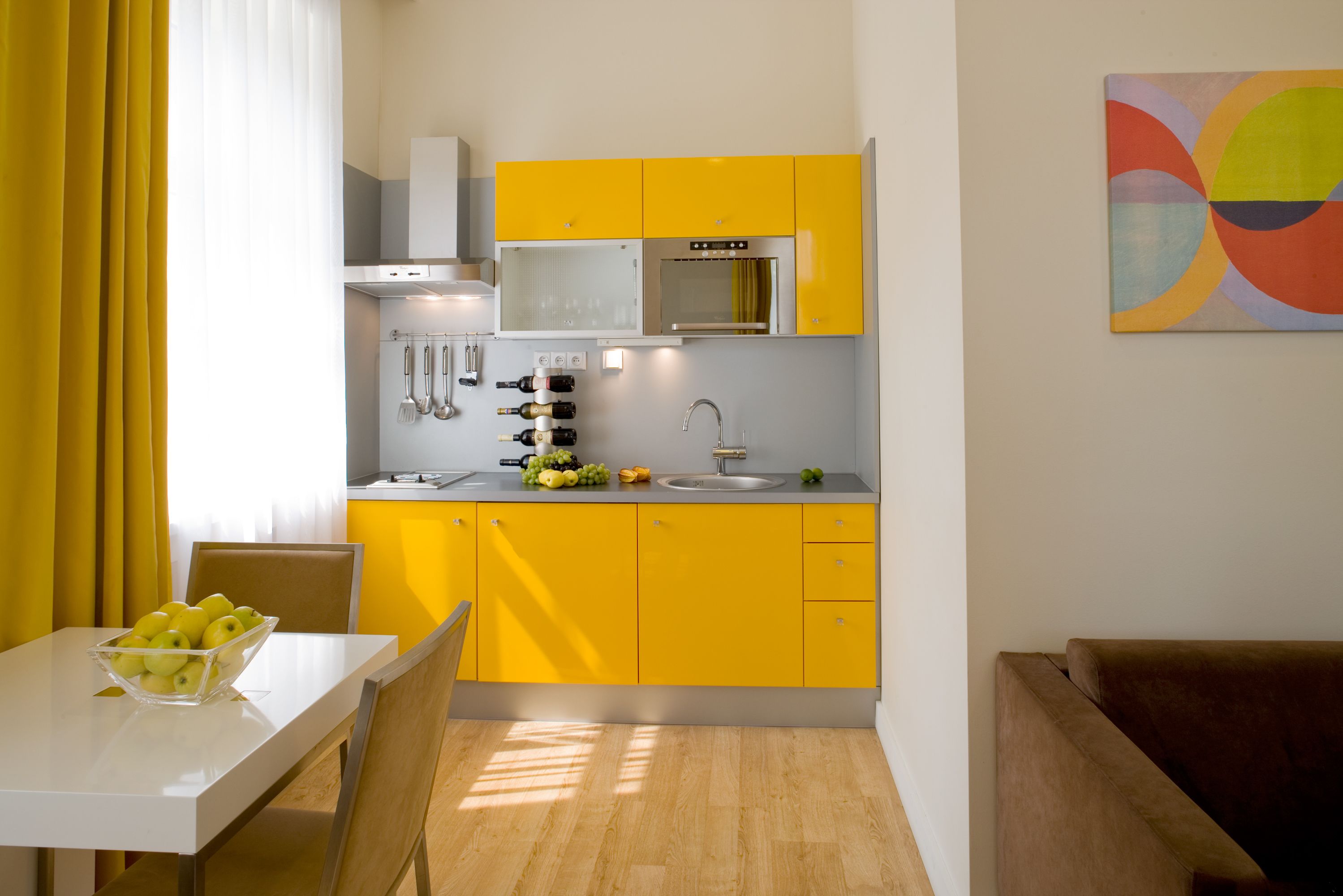 A modern kitchen with yellow cabinets, a white countertop, and a dining area with a table and chairs.