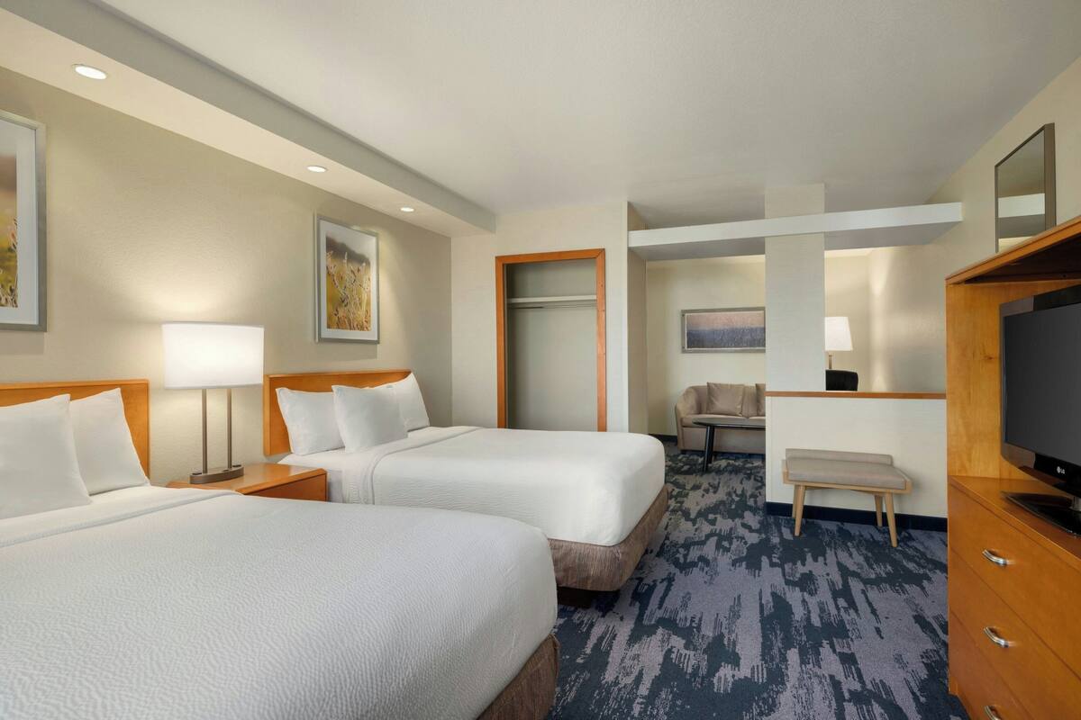 A hotel room with two beds, a desk, a chair, a TV, and a door leading to a bathroom.