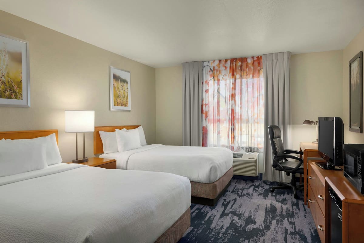 A hotel room with two beds, a desk, a chair, a television, and a window with curtains.