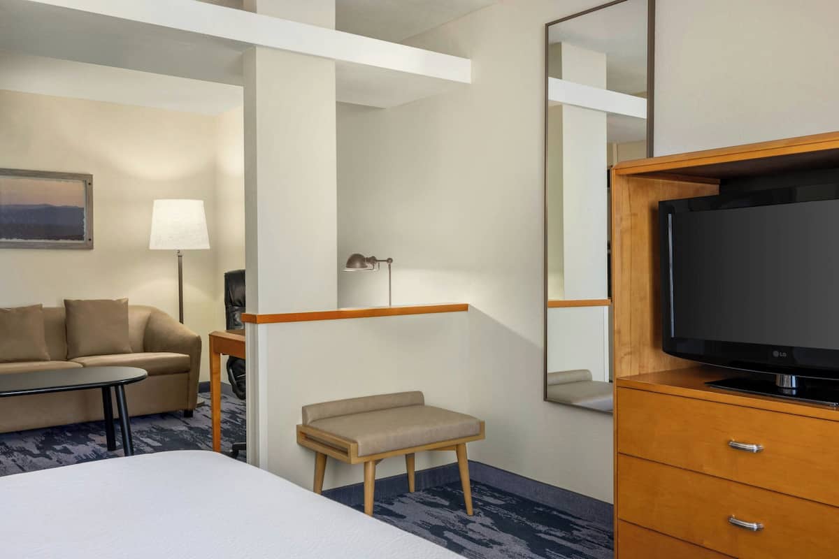 A hotel room with a bed, a TV on a wooden cabinet, a small table, a sofa, a lamp, and a mirror.
