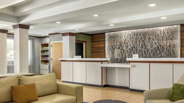 A reception area with a reception desk, a sofa, a coffee table, and a decorative wall. - Fairfield Inn & Suites by Marriott Springdale (Springdale)