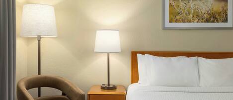 Habitación de hotel con una cama, dos lámparas de noche, una silla y un cuadro en la pared.