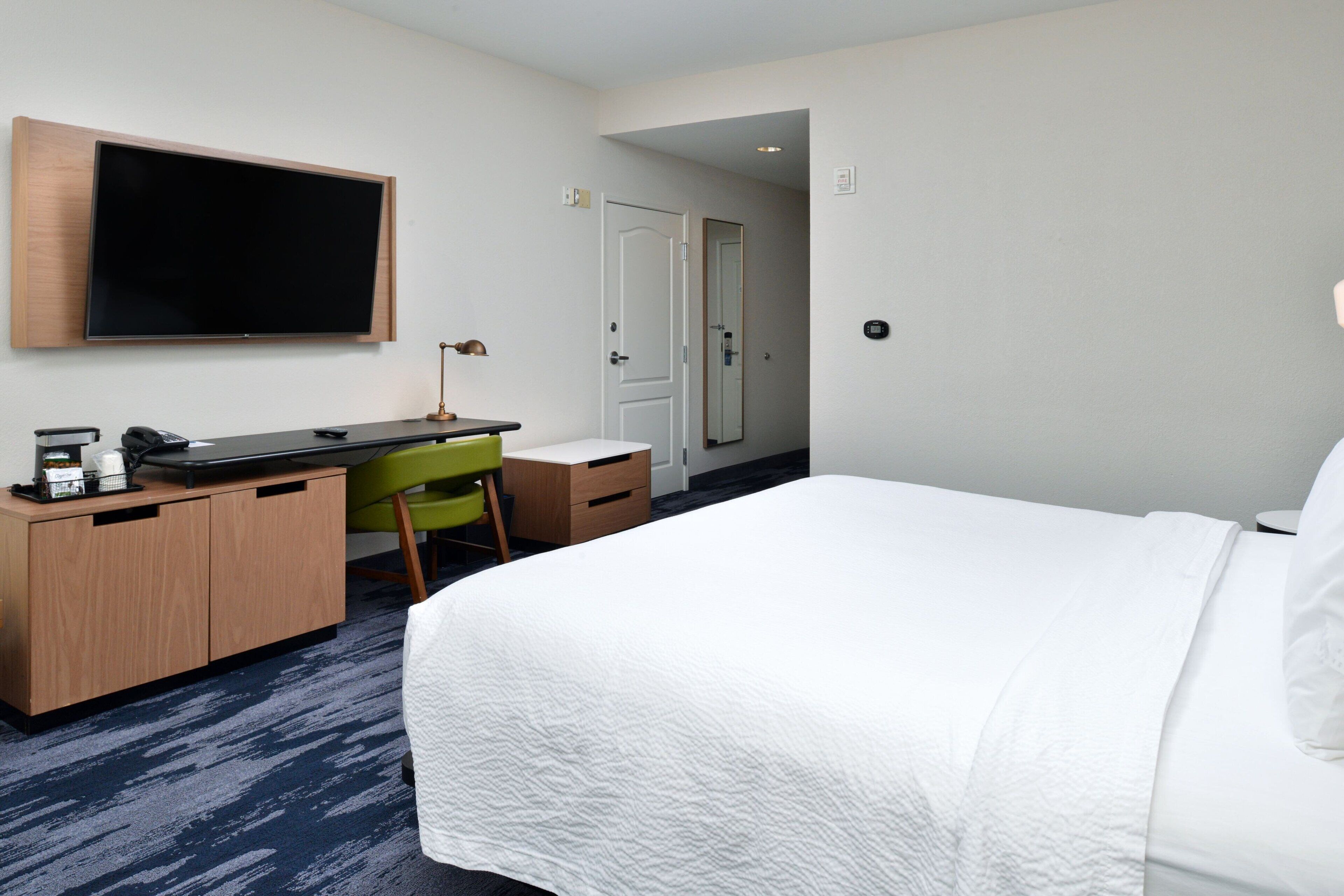A hotel room with a bed, a desk with a chair, a television, and a door.