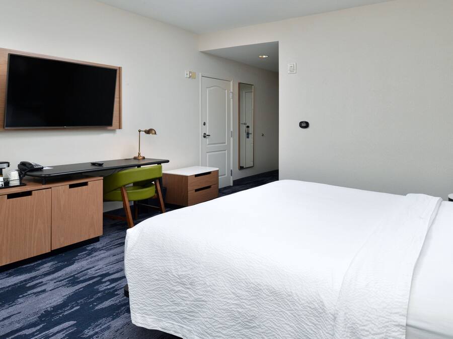 A hotel room with a bed, a desk with a chair, a television, and a door.