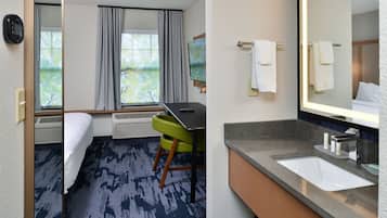 A hotel room with a bed, a desk, a chair, a large window with curtains, a flat-screen TV, a bathroom with a sink, mirror, and towel rack.
