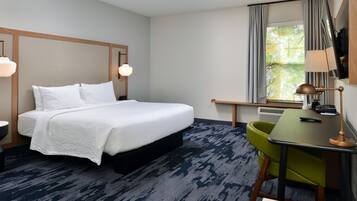 A hotel room with a bed, a desk, a chair, a lamp, and a window with curtains.