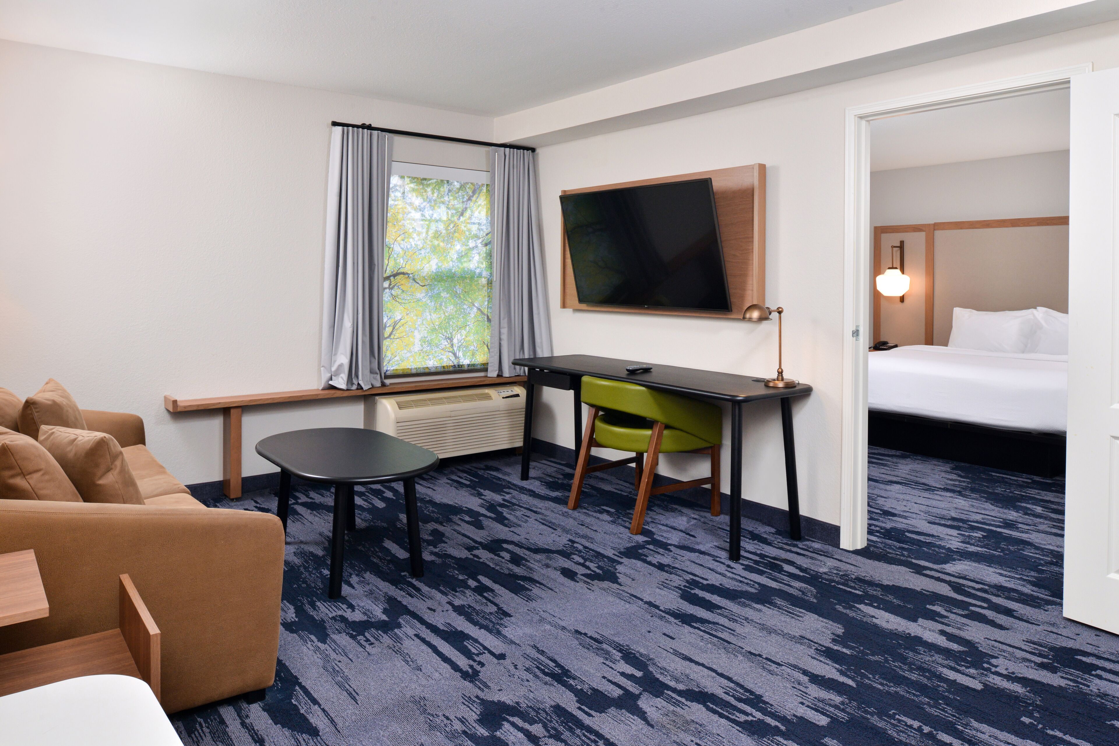 Une chambre d’hôtel comprenant un lit, un bureau avec une chaise, une télévision, une fenêtre avec des rideaux et une vue sur les arbres.