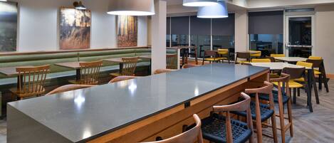 A modern restaurant with a long counter, wooden chairs, and pendant lighting.