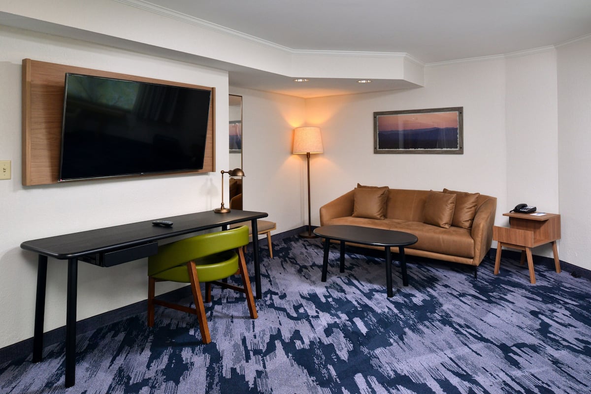 Une chambre d’hôtel équipée d’un téléviseur à écran plat fixé au mur, d’un bureau avec une chaise, d’un canapé, d’une lampe et d’une petite table.