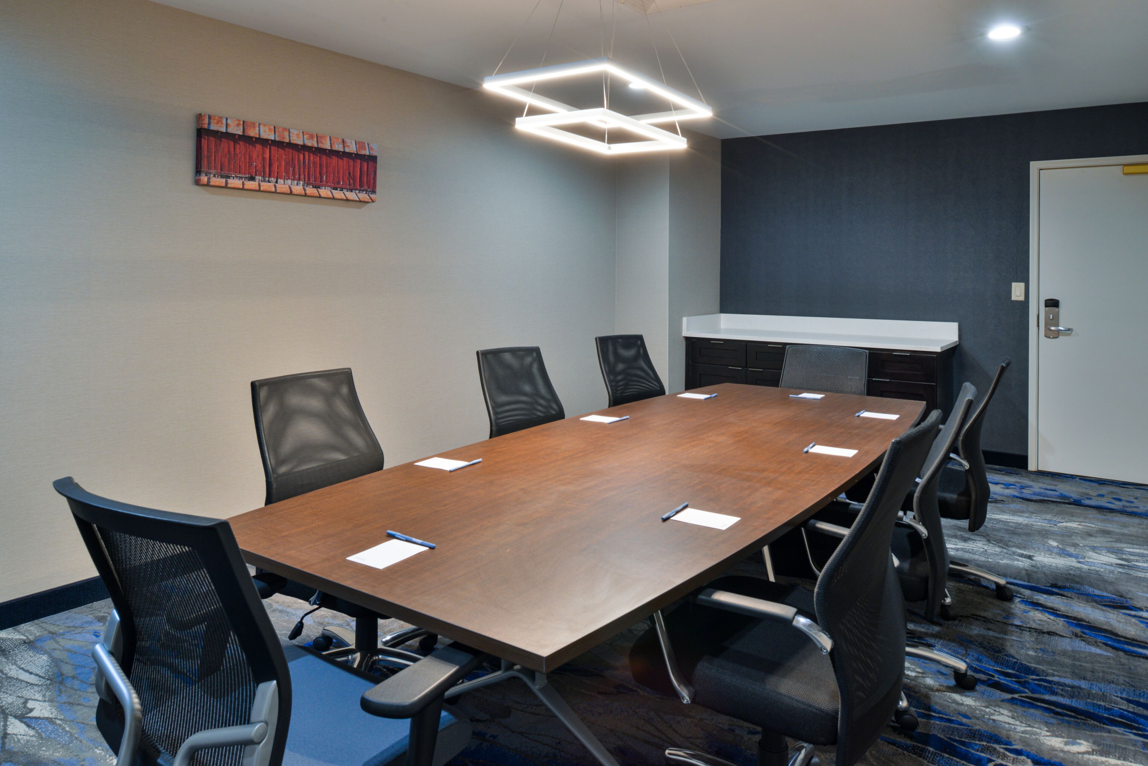 A conference room with a long table, six chairs, a whiteboard, and a door.
