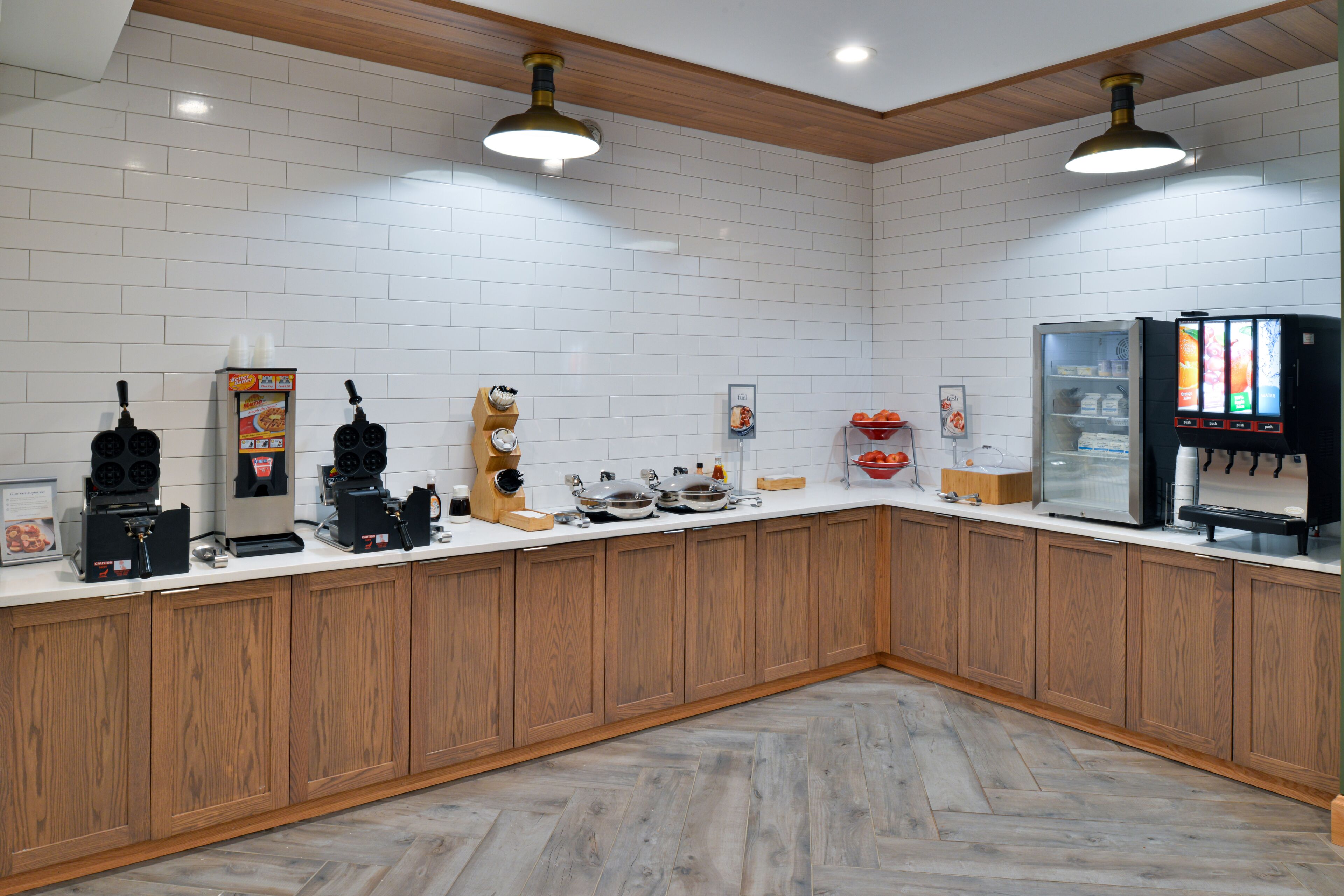 A modern kitchen with white tiled walls, wooden cabinets, and a herringbone-patterned floor.