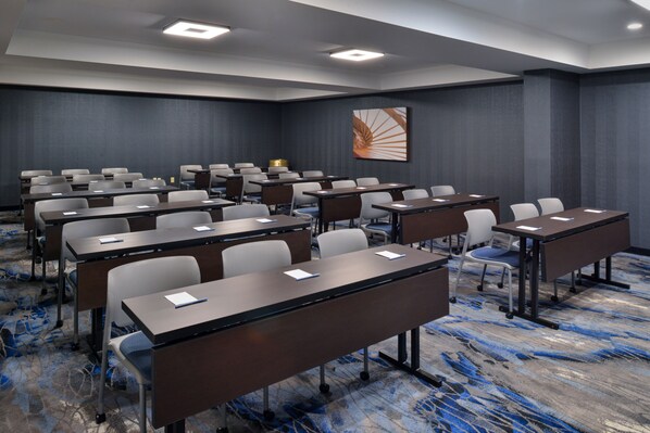 A conference room with rows of tables and chairs, equipped with laptops and papers, and a carpeted floor.