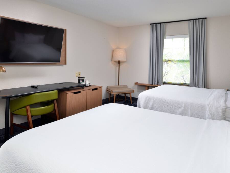 A hotel room with a large bed, a desk with a chair, a television, a lamp, and a window with curtains.