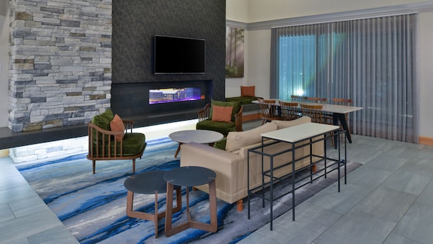 Una sala moderna con pared de acento de piedra, televisor de pantalla plana y chimenea. Hay varias opciones de asientos, incluyendo un sofá, sillas y una mesa.