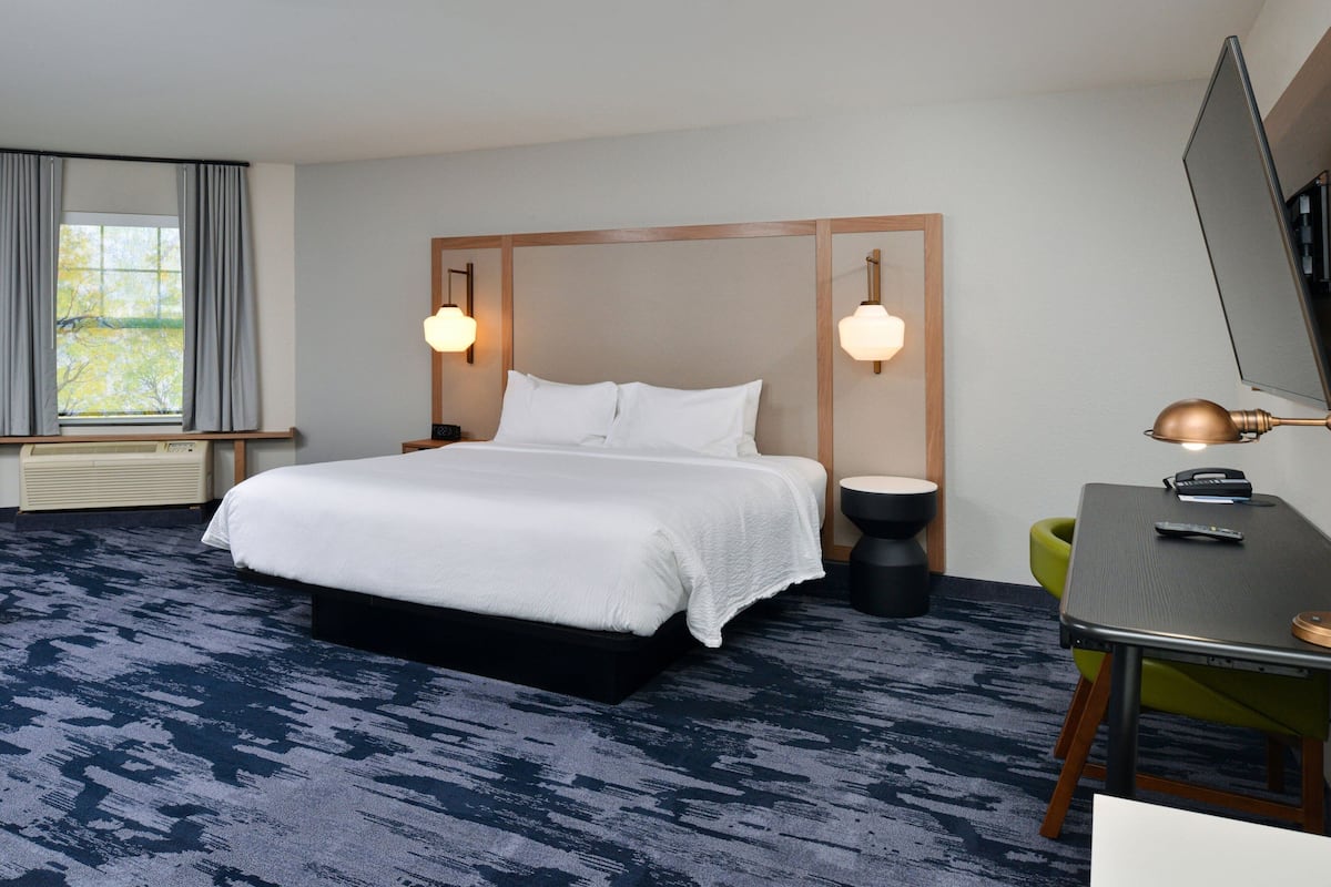 Une chambre d’hôtel avec un grand lit, un bureau, une chaise, un miroir et une fenêtre avec des rideaux.