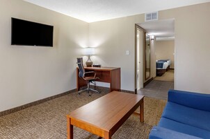 A hotel room with a wooden desk, a blue sofa, a flat-screen TV mounted on the wall, and a lamp on the desk.