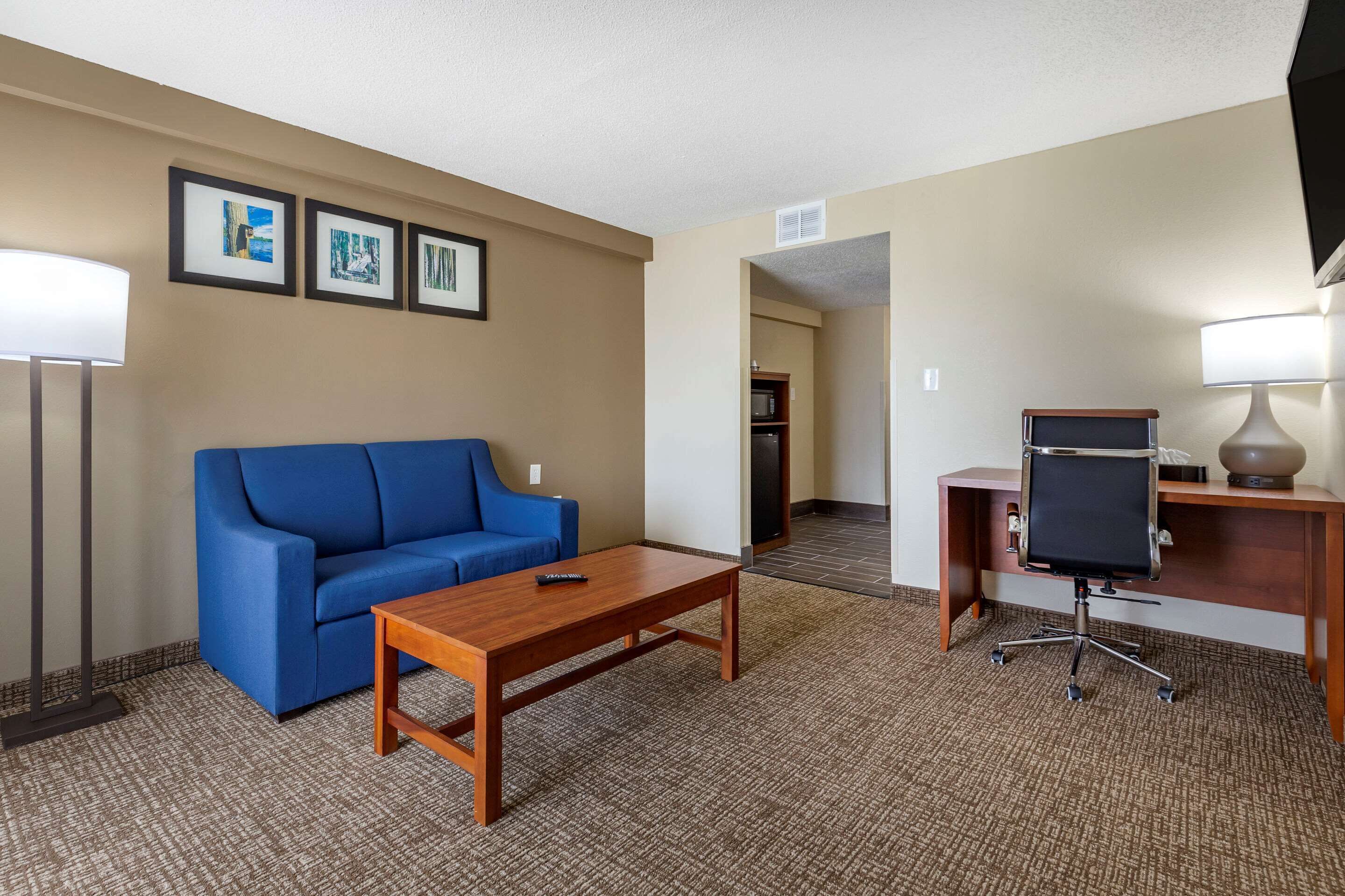 A hotel room with a blue sofa, a wooden coffee table, a desk with a chair, and a TV on a stand.