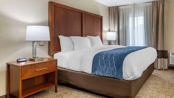 A hotel room with a large bed, wooden headboard, two bedside lamps, a nightstand, and a window with curtains.