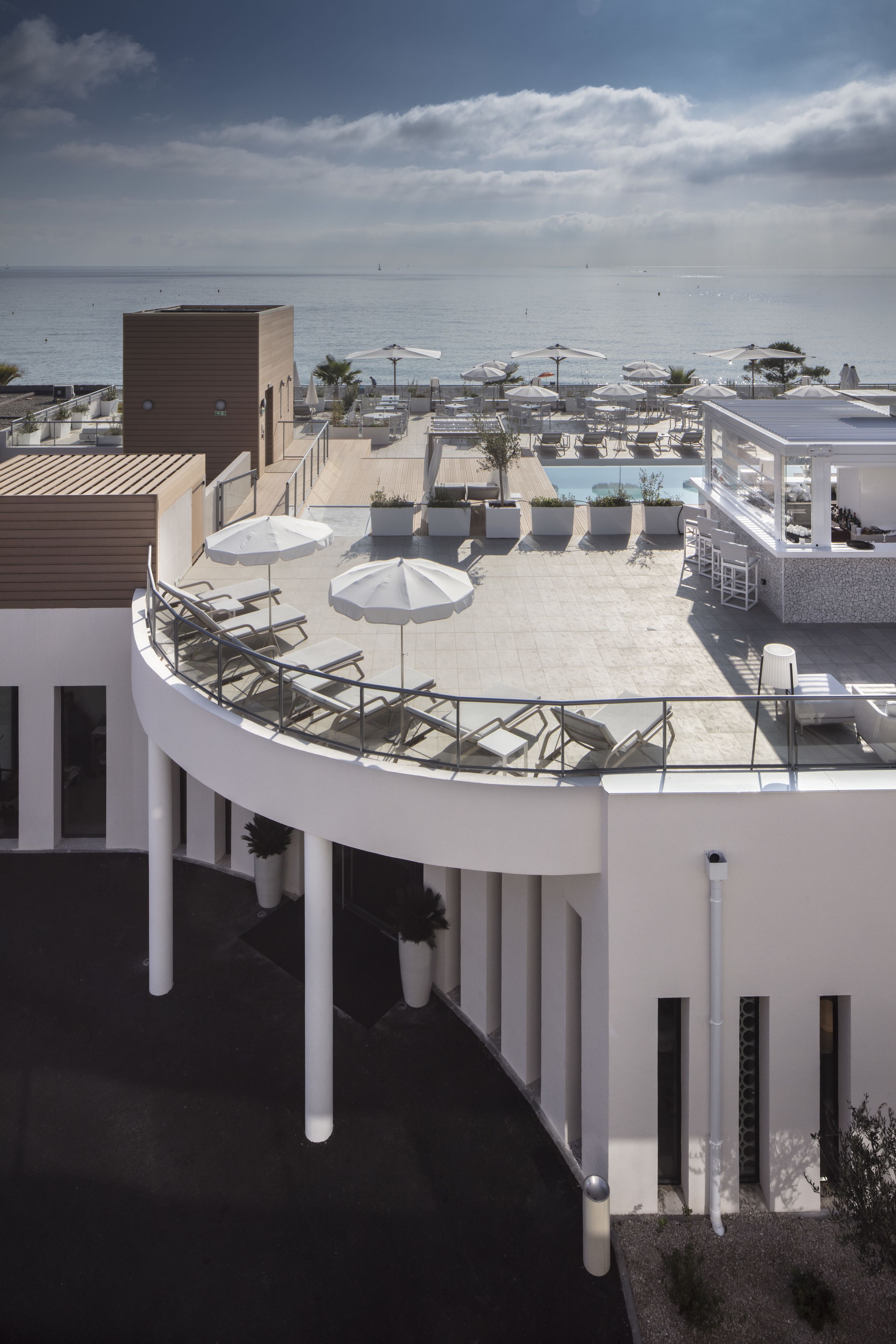 Une terrasse sur le toit, dotée de chaises longues et de parasols, offrant une vue sur une piscine et l’océan.