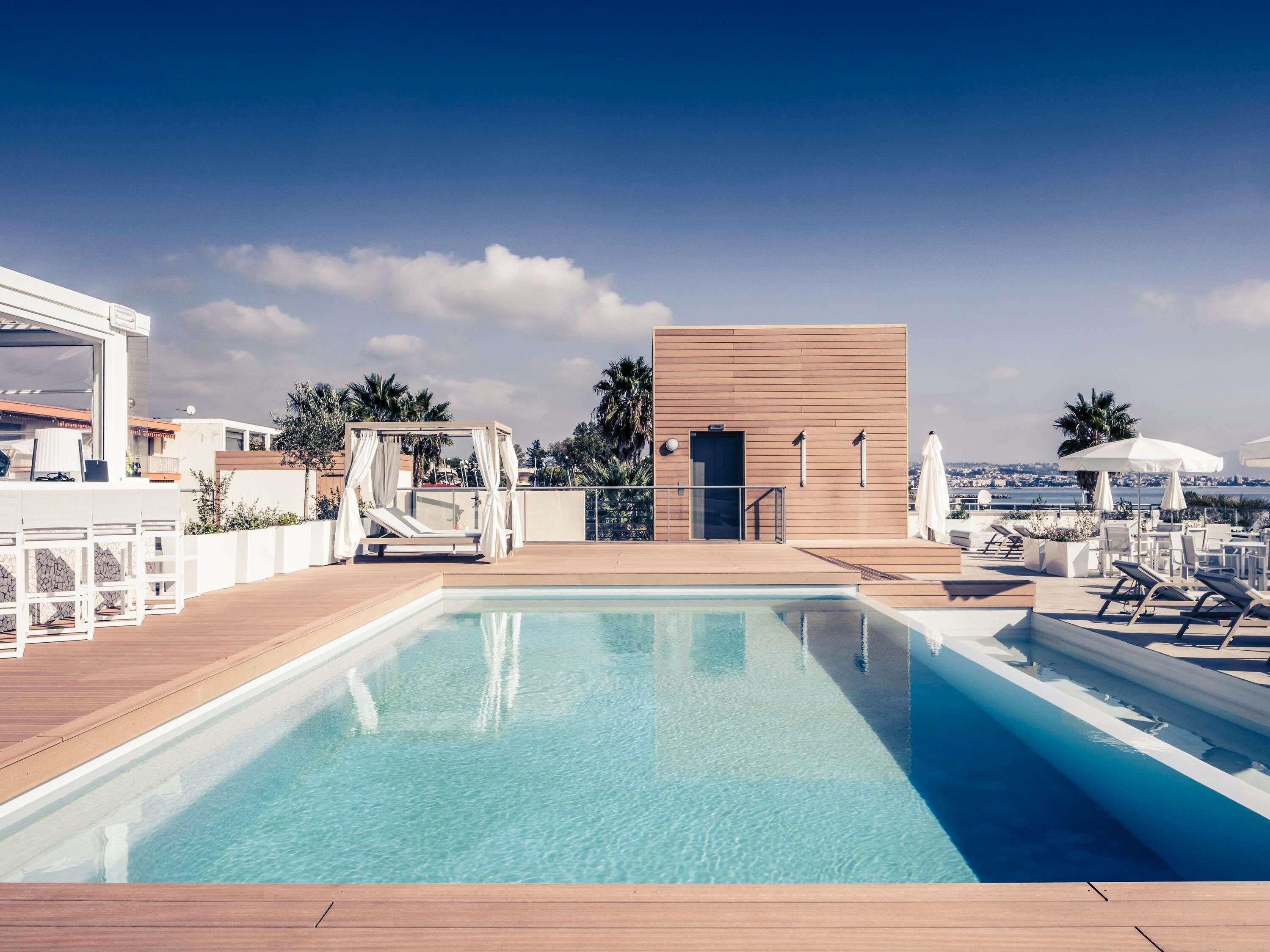 Un área de piscina con terraza de madera, un toldo y sillas de descanso.