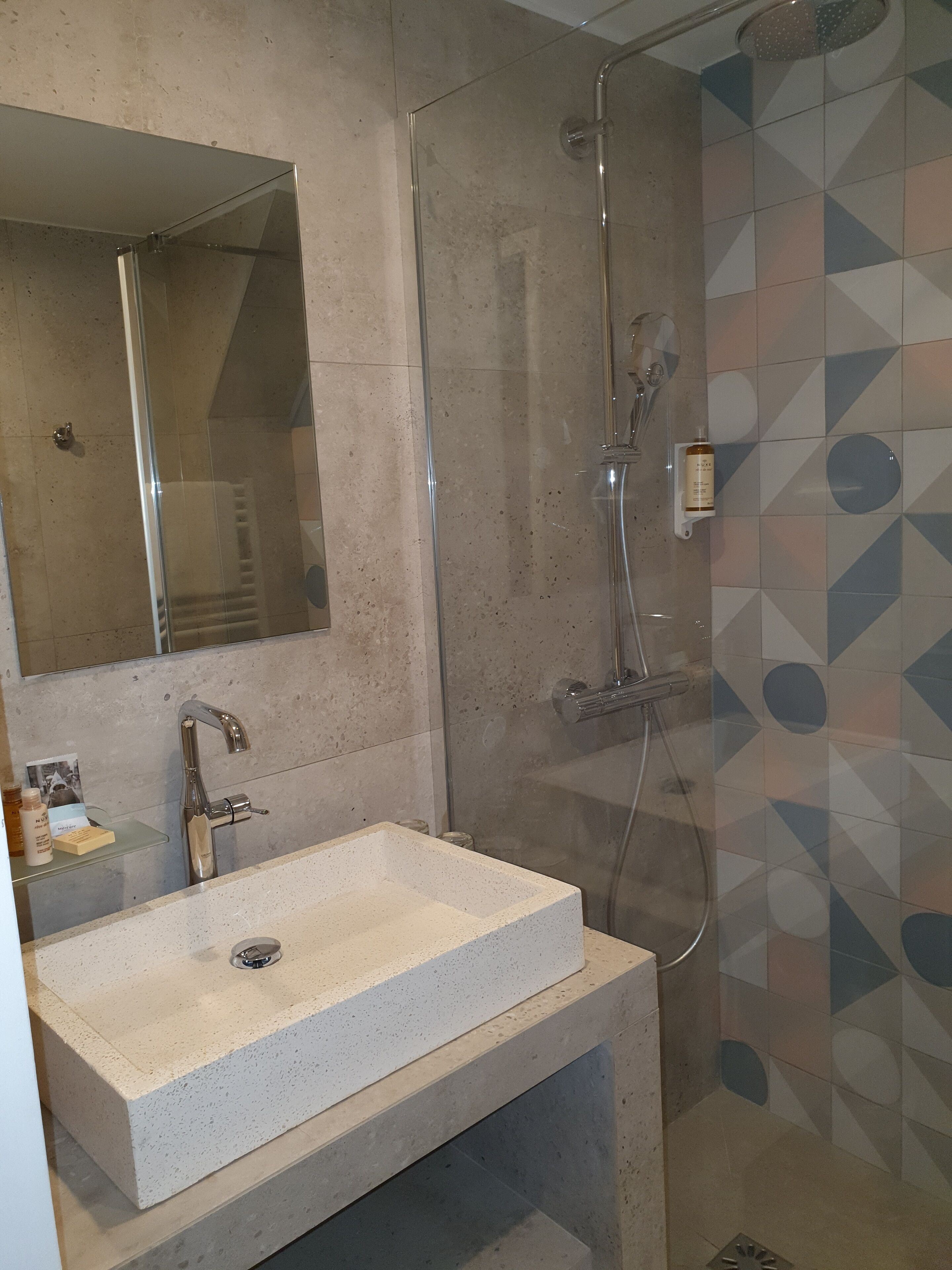 A bathroom with a glass-enclosed shower, a sink with a mirror above it, and tiled walls with a geometric pattern.