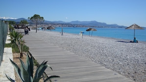 A pebble beach with a wooden walkway, beach umbrellas, and a clear view of the sea and distant mountains. - Mercure Villeneuve Loubet Plage (Villeneuve-Loubet)
