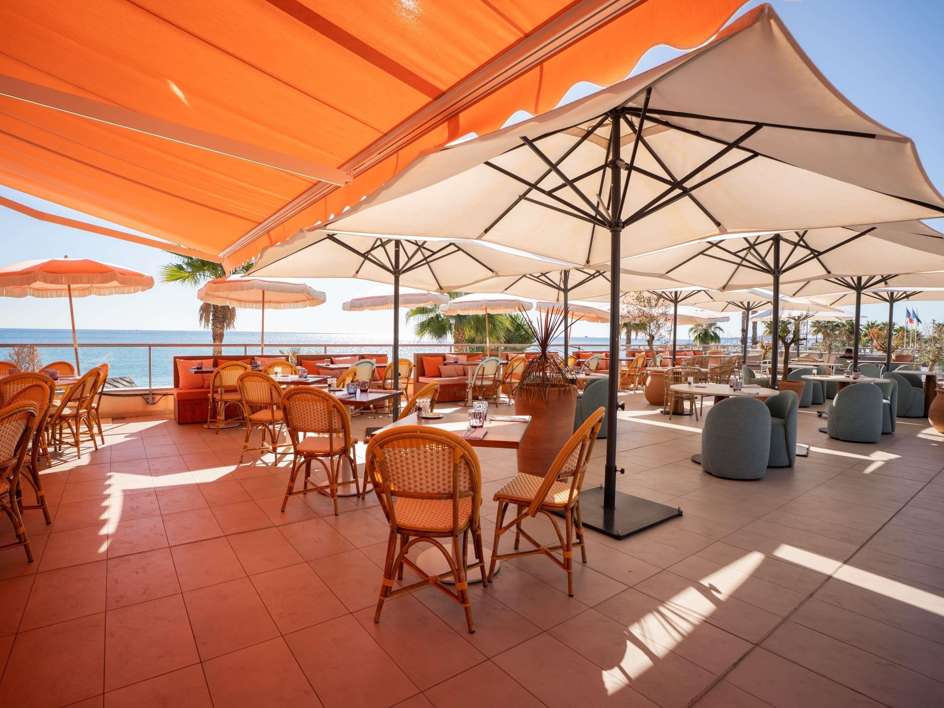 Un espacio al aire libre con mesas, sillas, sombrillas y vistas al mar.