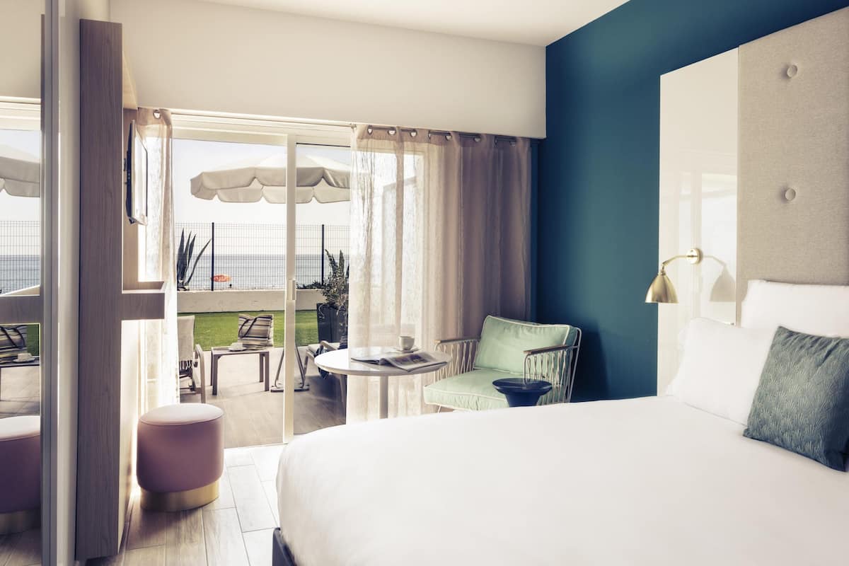 Une chambre d’hôtel avec un grand lit, un balcon doté d’un espace salon extérieur et une vue sur la mer.