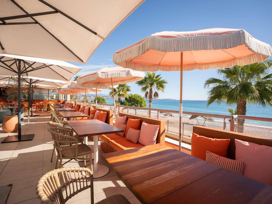 An outdoor seating area with tables and chairs, umbrellas, and a view of the beach.