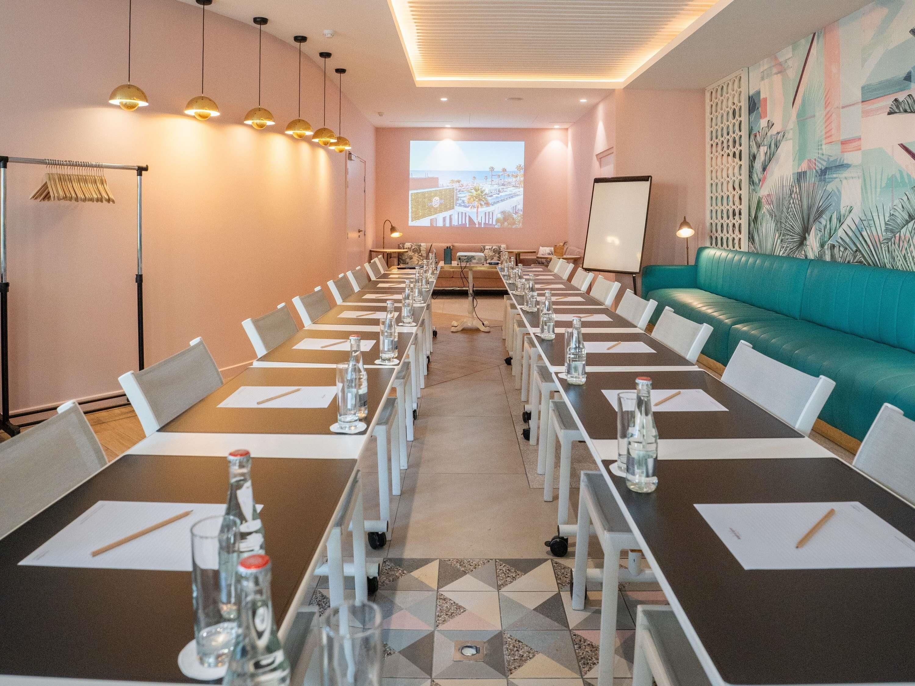 Une salle de conférence équipée d’une longue table, de chaises, d’un écran de projection et d’un canapé de couleur turquoise.