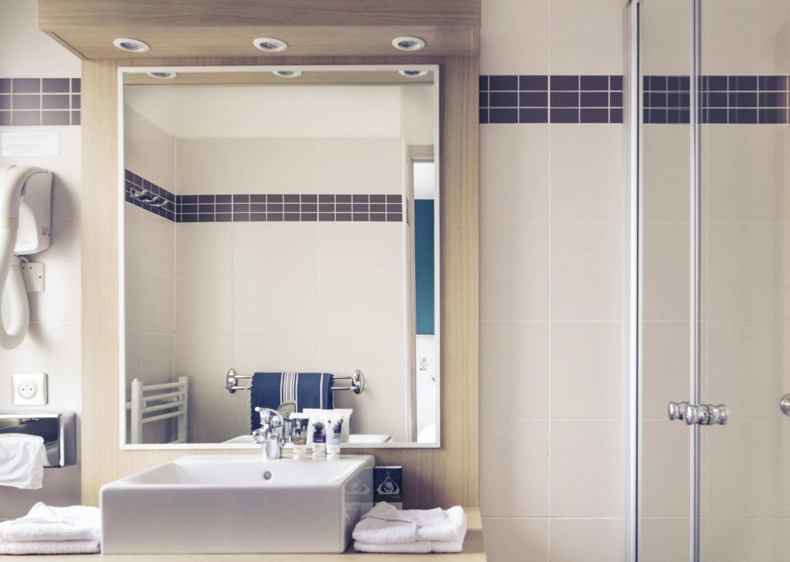 A bathroom with a sink, mirror, towel rack, and a shower area.