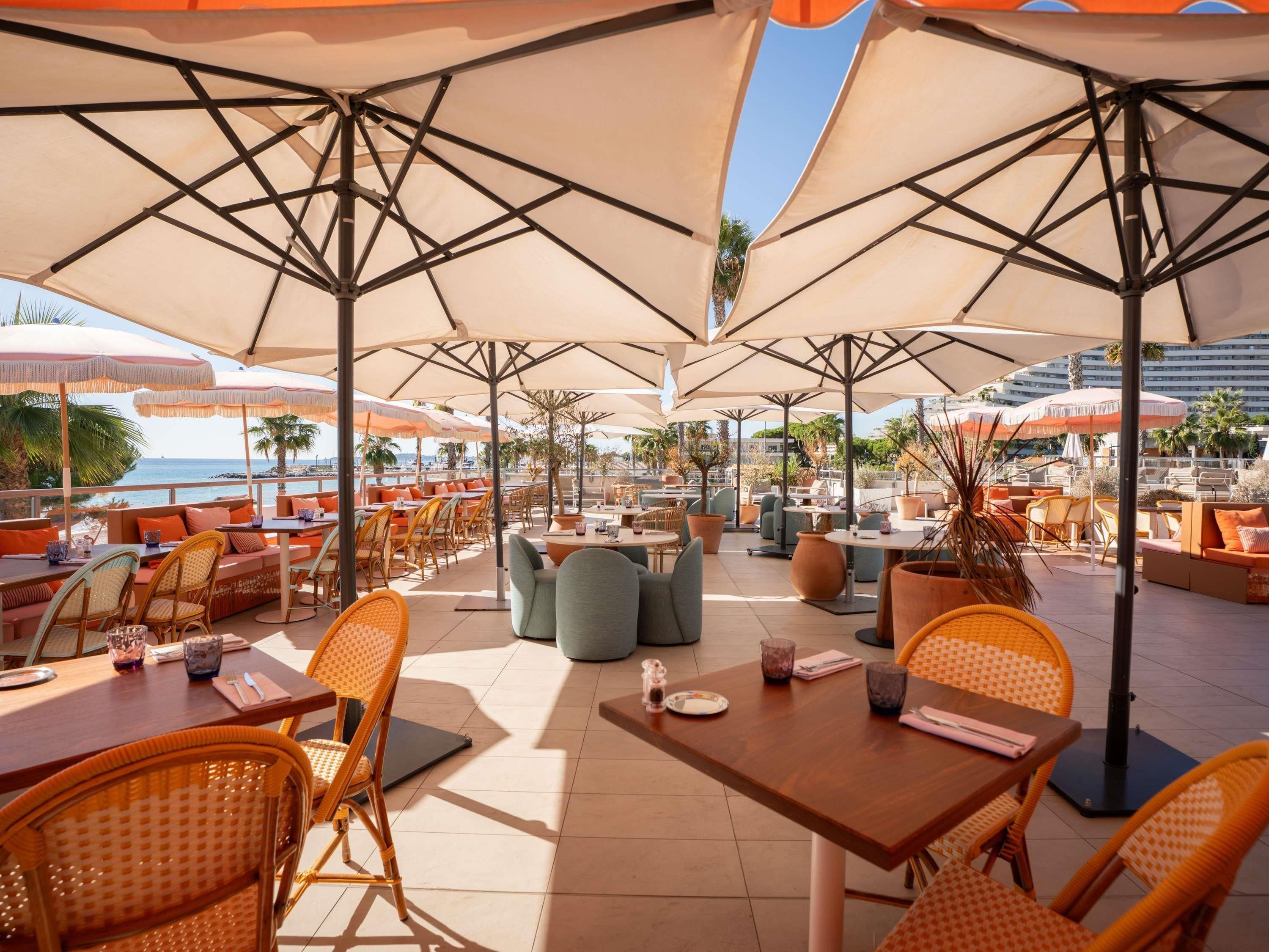 An outdoor seating area with tables and chairs, umbrellas, and a view of the sea.