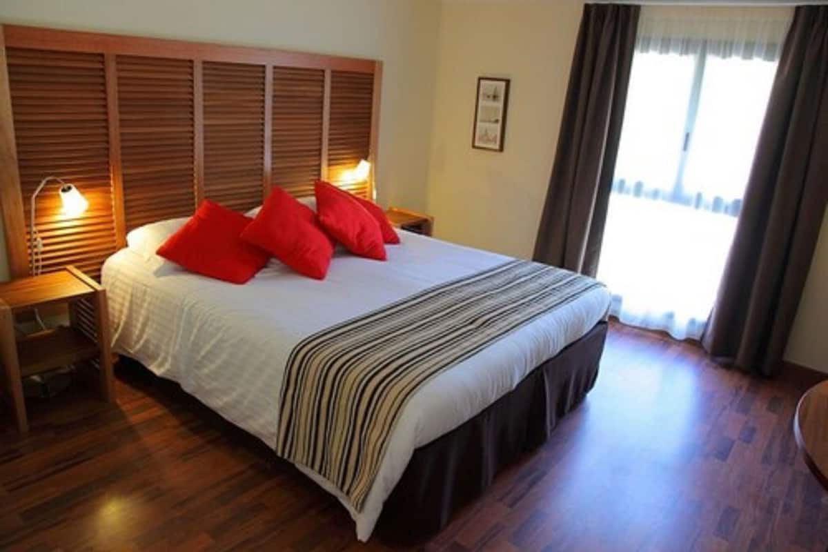 Ein ordentlich gemachtes Bett mit einer gestreiften Decke, zwei roten Kissen und einem hölzernen Kopfteil.
