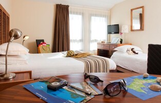 Habitación de hotel con dos camas, un escritorio con computadora, un televisor y una ventana con cortinas.