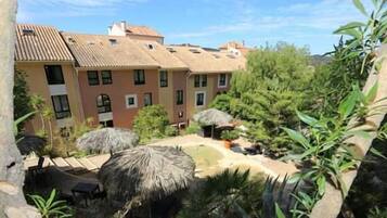 A hotel with multiple buildings, outdoor seating areas with thatched umbrellas, and lush greenery.